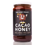 Raw Honey Project Cacao Honey jar front label — one pound of chocolate-infused raw honey made with four real ingredients: raw honey, cacao, organic vanilla bean, and pink salt. Label reads ‘delicious chocolate,’ ‘dairy and nut free,’ and ‘no refined sugar or oil.’