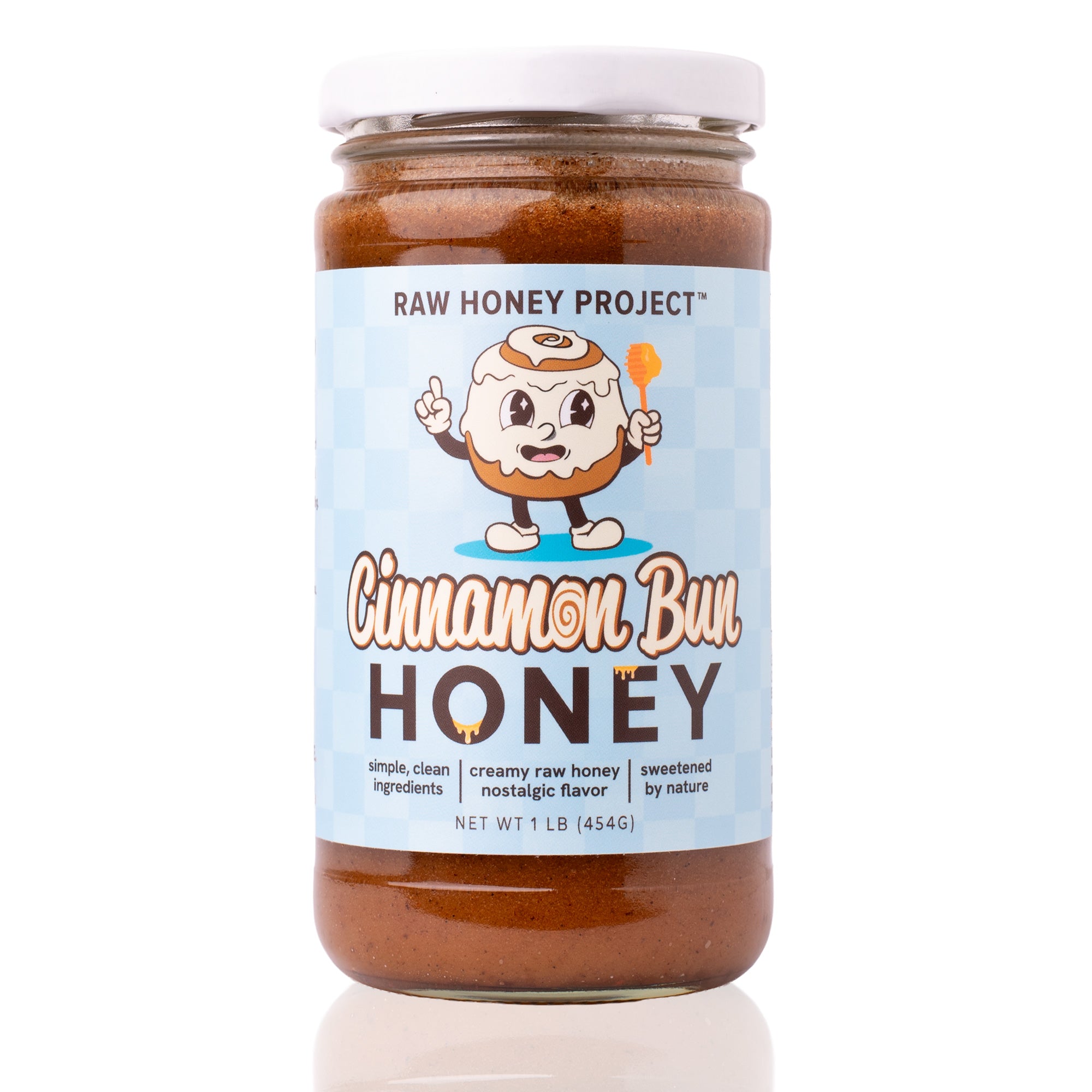 Glass jar of Raw Honey Project Cinnamon Bun Honey, 1 lb, with a smiling cartoon cinnamon roll mascot holding a honey dipper on a light blue checkered background. Creamy brown raw honey visible inside.