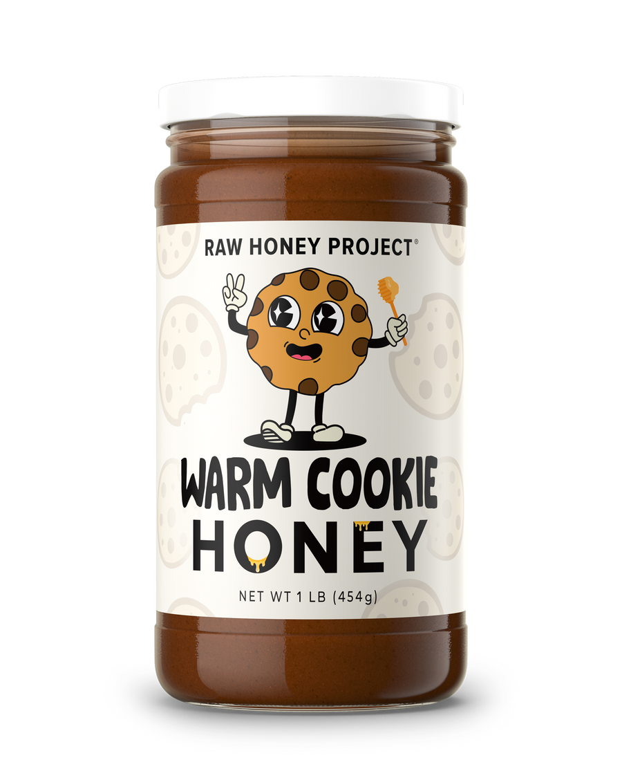 A jar of Raw Honey Project Warm Cookie Honey, featuring a white label with a cartoon cookie character and bold black text, set against a plain white background.